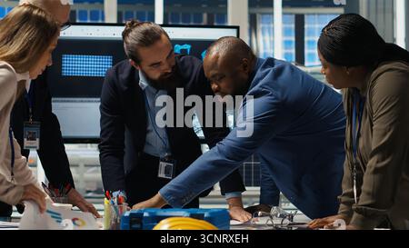 Factory management looking over schematics, working together to expand production. Industrial plant executives doing brainstorming, discussing over blueprint of facility layout, camera B Stock Photo