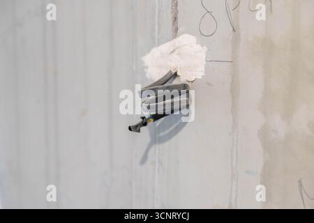 Cables wires sticking out of grey concrete wall. Details during house renovations. Stock Photo