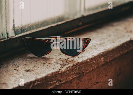 Stylish cat eye sunglasses resting on a weathered windowsill. A pair of tortoiseshell glasses sits on a rustic sill with a window in the background, c Stock Photo