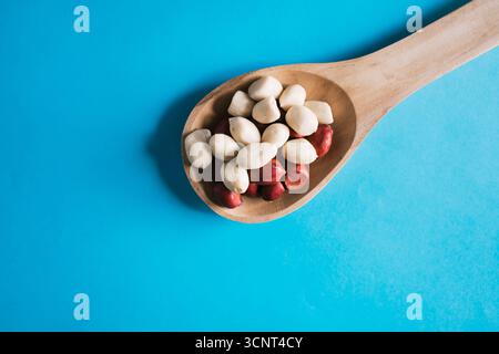 Peanuts with red shell scattered on a blue surface and a wooden spoon Stock Photo