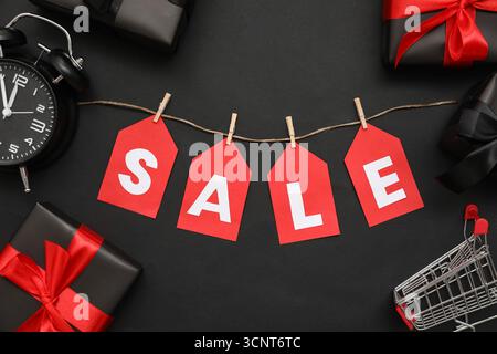 Composition with word SALE, gifts, alarm clock and small shopping cart on dark background Stock Photo