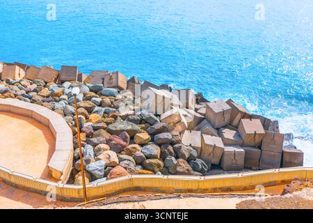 Blue ocean meets a unique breakwater of rocks and concrete blocks, creating striking coastal scene. Image captures power of sea and human engineering Stock Photo