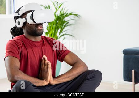 White VR headset and headphones lying on wood floor near potted plant and blue ottoman Stock Photo