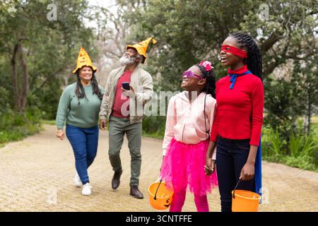 Diverse family walking along park path wearing orange hats and holding pumpkin buckets, copy space Stock Photo