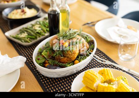 Roasted chicken is resting in casserole dish on wooden table with corn, beans and mashed potatoes Stock Photo