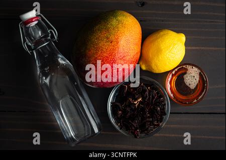 Iced Mango Hibiscus Tea Ingredients: Fresh mango, dried hibiscus flowers, honey, lemon, and water on a rustic wooden table Stock Photo
