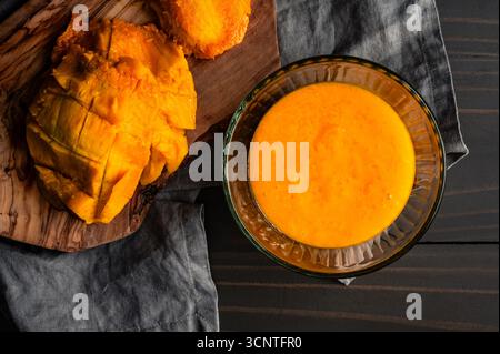 Homemade Mango Puree in a Glass Bowl: Pureed tropical fruit with mango peel and seed on a wooden cutting board Stock Photo