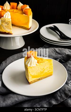 Slice of Mango Mousse Cake on a Plate Angled View: Piece of swirled mousse cake with with a stack of plates, forks, and cake stand in the background Stock Photo