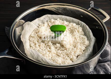 Soaked Glutinous Rice in a Cheesecloth-Lined Steamer Basket: Uncooked sticky rice inside a food steamer insert lined with muslin gauze in a saute pan Stock Photo