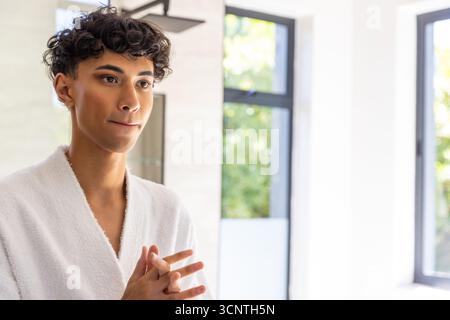 Middle eastern man applying skincare product in bathroom with bathrobe and framed windows Stock Photo