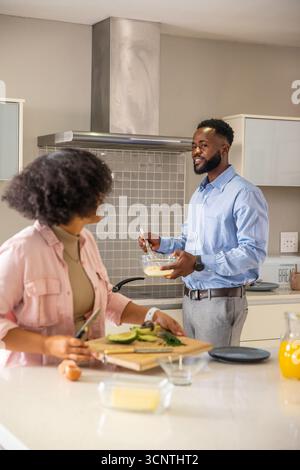 Couple whisking eggs in glass bowl, slicing avocado on cutting board in kitchen, copy space Stock Photo