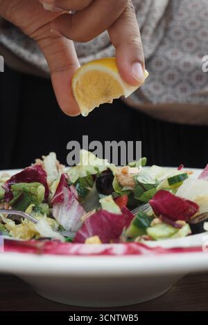 Squeezing lemon over fresh salad in outdoor setting Stock Photo