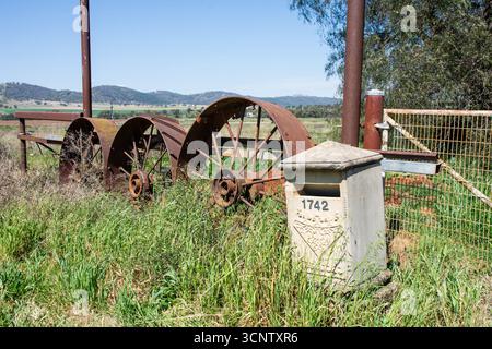 Farm entry with three old rusty iron spoked machinery wheels and a stone mailbox near Barraba NSW Australia. Stock Photo