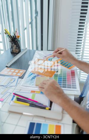 A focused designer is working on UX/UI design ideas, analyzing color palettes and interface structures pinned on a board. The scene reflects creativit Stock Photo