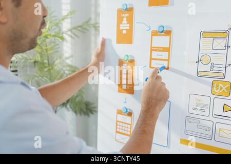 A young designer is working on a UX UI project, analyzing mobile app wireframes and choosing color palettes on a whiteboard. He focuses on brainstormi Stock Photo