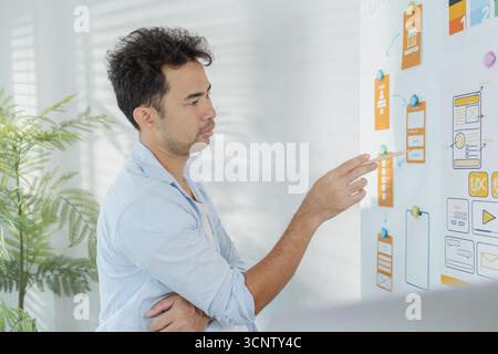 A creative designer is working on UX UI planning, reviewing wireframes, and adjusting color schemes for a mobile application project, showing focus an Stock Photo