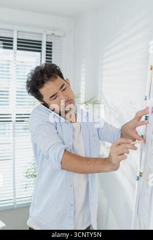 A creative designer works on UX/UI planning, analyzing sketches and prototypes on a whiteboard while using a laptop. The process shows design thinking Stock Photo