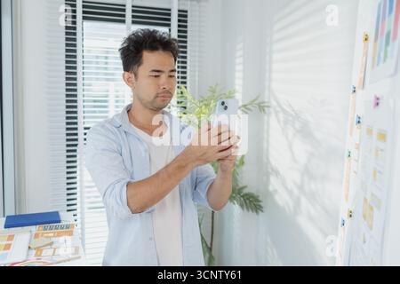 A creative designer works on UX/UI planning, analyzing sketches and prototypes on a whiteboard while using a laptop. The process shows design thinking Stock Photo