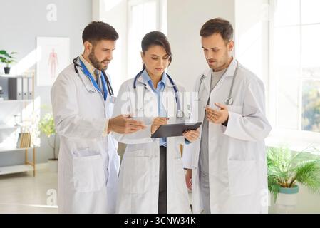 Three medical professionals share ideas and discuss patient care strategies while working in clinic. Stock Photo