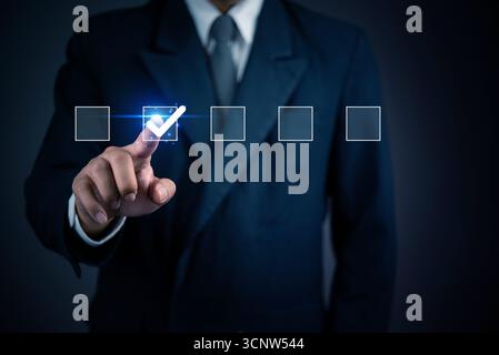 Businessman selecting checklist box on virtual screen. Concept of goal setting, decision making, and digital task management for business success. Stock Photo