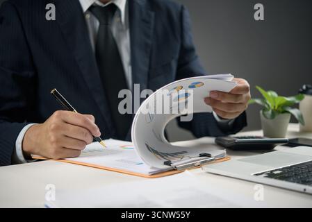 Businessman analyzing financial report with charts and graphs at office desk. Concept of data analysis, business strategy, and company performance rev Stock Photo