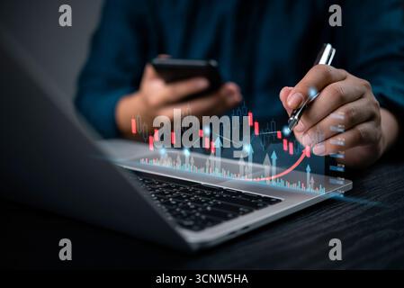 Businessman analyzing stock market data analysis with digital charts on laptop and smartphone, financial trends, forex trading strategies, and investm Stock Photo
