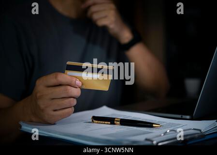 Man holds credit card online payment or financial transaction, with a laptop and documents on the desk. digital finance, secure e-commerce, and busine Stock Photo