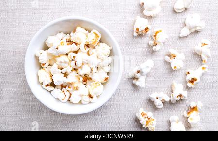 Popcorn, popped corn in a white bowl on linen. Seeds of the Zea mays variety everta, expanded and puffed up, after heated. Snack food. Stock Photo