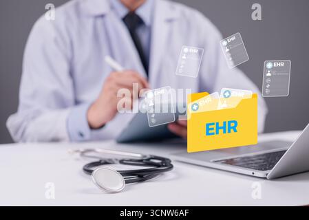Doctor using digital tablet with EHR folder icon and medical records floating above laptop, representing electronic health records and modern healthca Stock Photo