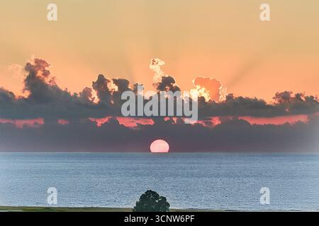 A radiant sunrise emerges above the sea, with glowing clouds and warm colors creating a peaceful, dreamlike atmosphere over the water. Stock Photo