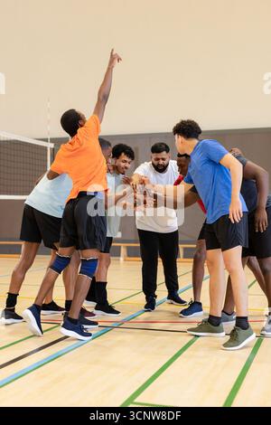 Diverse male volleyball players huddling at gym under net stacking hands wearing knee pads Stock Photo