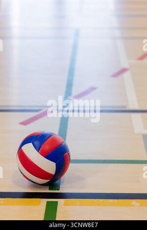 Colorful volleyball resting on gym floor near intersection of colored court lines Stock Photo