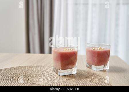 Two glasses filled with a vibrant banana-strawberry smoothie are placed on a light wooden table Stock Photo