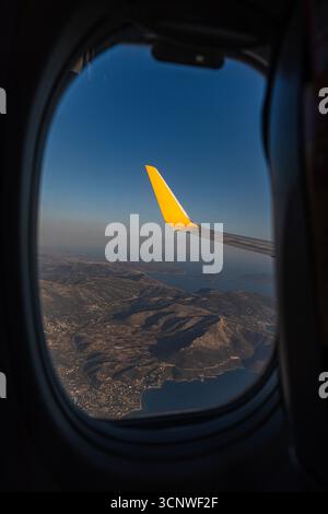 A picturesque view from an airplane window reveals the vast landscape below and the airplane's wing slicing through the clear blue sky, capturing the Stock Photo