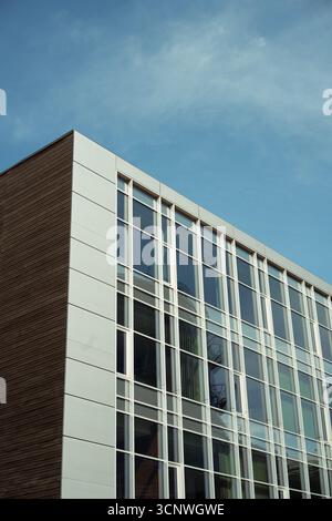 An angular view of a modern glass building showcasing sleek architectural design. The facade features clean lines and ample windows, under a clear blu Stock Photo