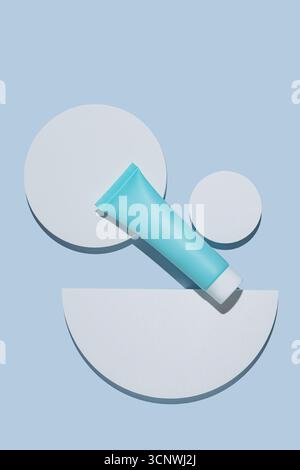 A chic cosmetic package featuring a blue tube on a minimalist blue background with geometric white shapes. Ideal for modern skincare or beauty product Stock Photo