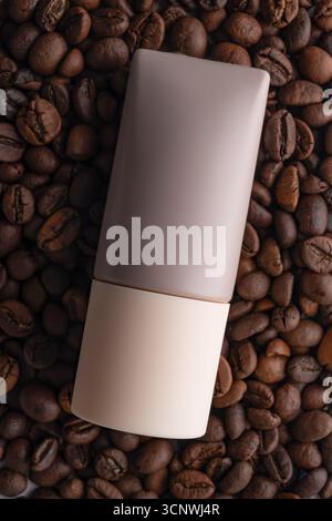A sleek cosmetic bottle infused with caffeine lies on a bed of roasted coffee beans, symbolizing the energizing and revitalizing effects of coffee bas Stock Photo