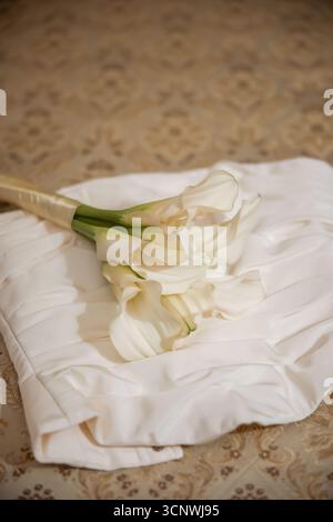A graceful arrangement of creamy white lilies elegantly placed on soft white fabric, capturing the essence of a romantic and sophisticated wedding set Stock Photo
