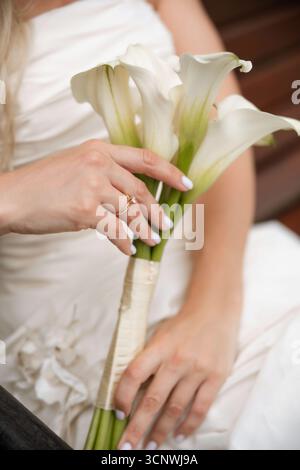 A close-up image of a bride holding an elegant bouquet of white flowers, showcasing her beautiful engagement ring on her finger, symbolizing love and Stock Photo