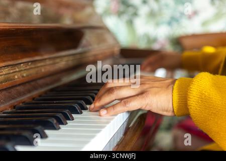 Close-up of a woman's hands playing the piano. She wears a yellow sweater, focusing intently on her practice in a warmly lit room, embodying art and p Stock Photo