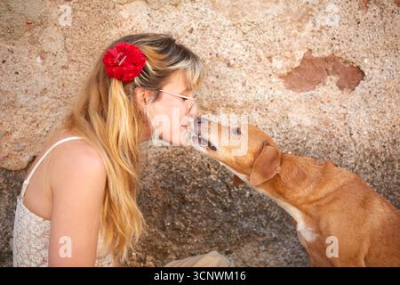 Close-up of a woman and her dog sharing a slice of cold cut meat, touching it from opposite ends. The playful and intimate scene captures trust, humor Stock Photo