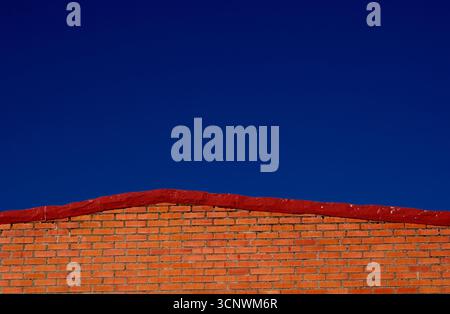 A bright red brick wall stands out against a clear blue sky. The vibrant colors create a striking contrast, highlighting the simplicity and beauty of Stock Photo