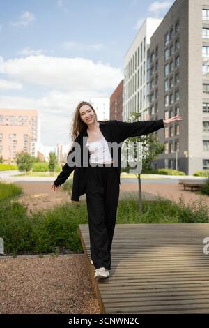 A young female biologist walks confidently through a landscaped urban setting, surrounded by modern buildings and greenery, embodying the harmony of s Stock Photo