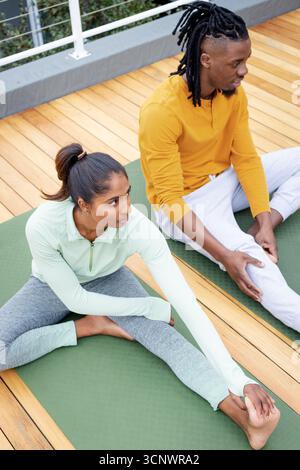 Indian woman and African American man practicing seated yoga on rooftop deck with green yoga mats Stock Photo