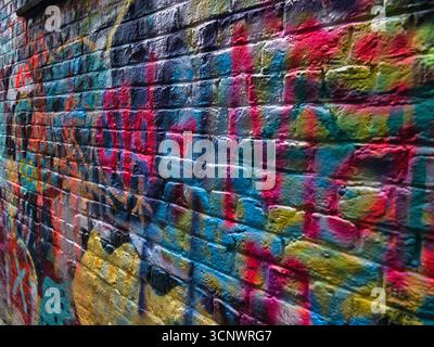 Macro of a Colorful Graffiti Wall - A detailed close-up of a brick wall covered in layers of vibrant, abstract graffiti and spray paint art. Stock Photo