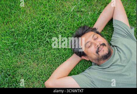 Top view portrait of handsome man with a beard relaxing lying on the grass. connecting to nature concept. Copy space. Stock Photo