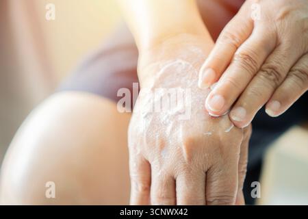 Senior woman hands applying cosmetic cream onto her hands at home, close-up and selective focus. Stock Photo