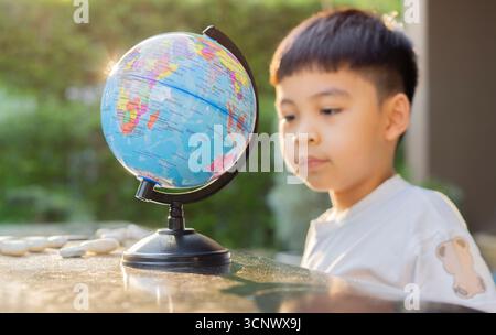 Happy Asian child boy looking at Globe global education world map while playing and joyfuling at outdoor. Kids Education concept. Selective focus. Stock Photo