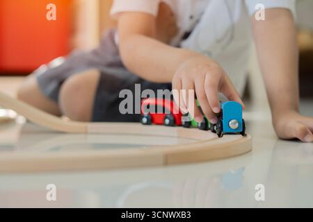 Close-up of wooden toys on the floor that the boy is playing with. A child lying on the floor rolls a train with colorful cars along a wooden railway. Stock Photo