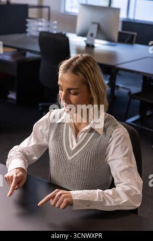 Woman pointing both index fingers downward at desk beside monitor in office workspace Stock Photo